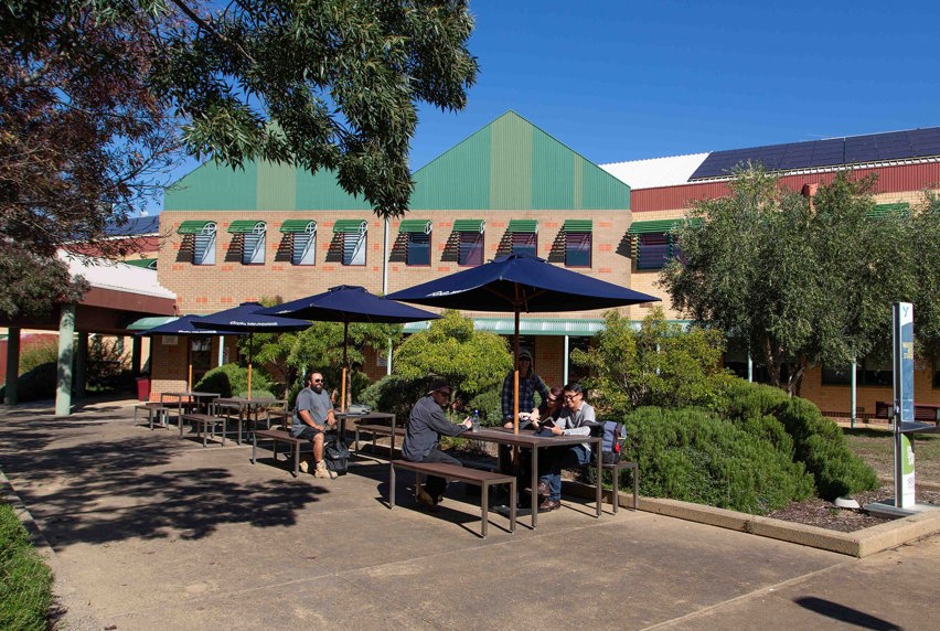 Epping courtyard with students sitting at bench under cafe umbrella on a sunny day