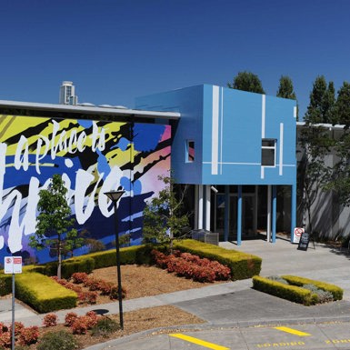 Facade of Greensborough campus. The entry is a blue building with a large mural that says "a place to thrive" on a blue, pink and yellow background